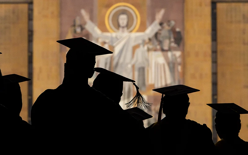 Silhouettes of graduating students wearing caps and gowns in front of the 'Word of Life' mural on Hesburgh Library inside Notre Dame Stadium at the University of Notre Dame.
