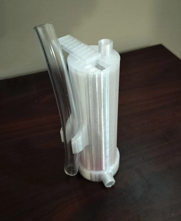 A 3D printed white plastic cylinder with a clear plastic tube inserted. A small, rectangular piece of white plastic is attached to the cylinder.