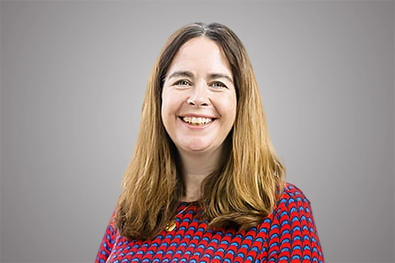 Woman with long brown hair smiles, wearing a red and blue patterned dress.