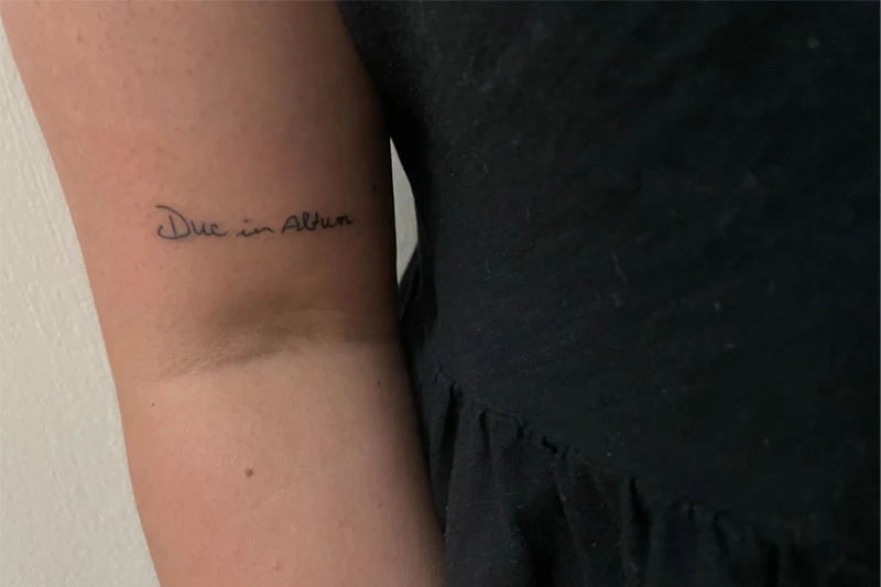 A tattoo on the inside of someone's arm reads 'Duc in Altum' in cursive black ink.