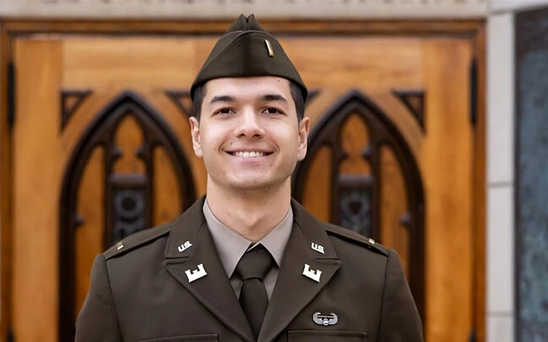Smiling ROTC cadet Stewart in U.S. Army service uniform stands in front of an ornate wooden door.