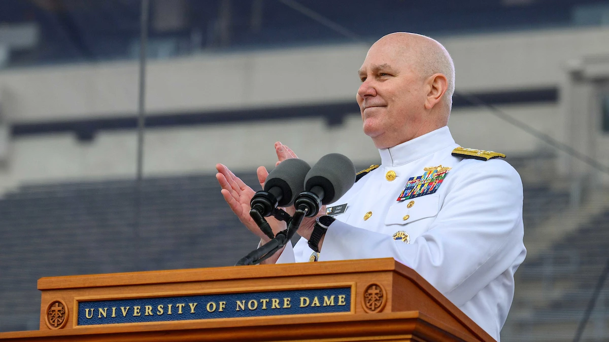 A military officer in a white dress uniform applauds at a podium bearing the University of Notre Dame logo.
