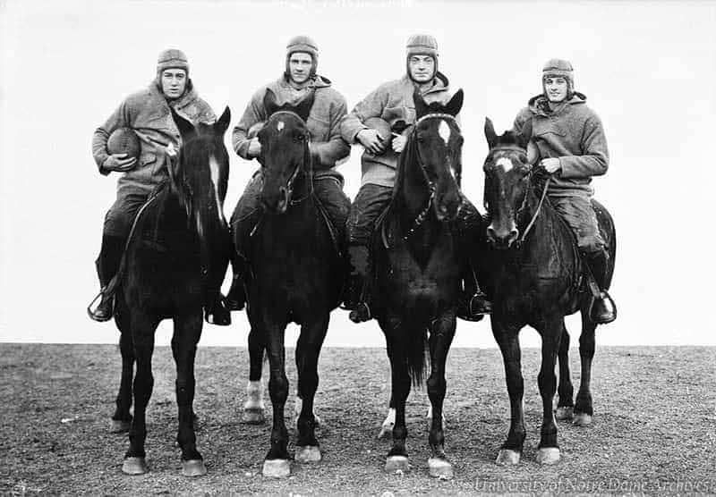 Four men holding a football, each on top of a black horse.