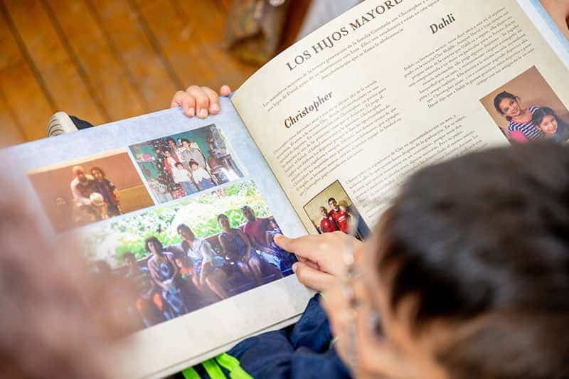 An opened book with text about a family's history with photos. A child's hand is pointing at one of the photos in the book.