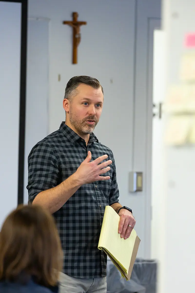 James Rudolph holding a notepad and speaking to a classroom on the campus of the University of Notre Dame.