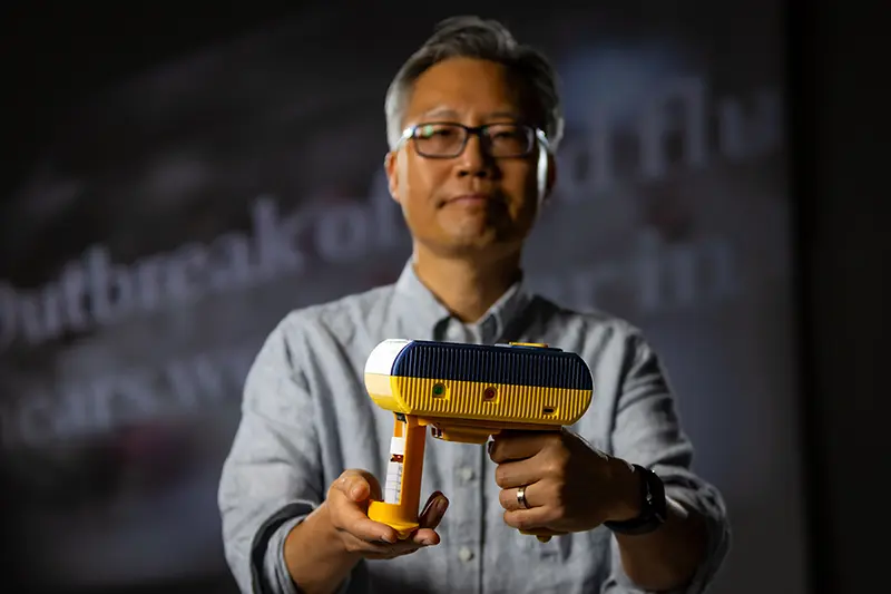 Nosang Myung holds the 'sniffer' device in front of an out-of-focus headline reading 'Outbreak of bird flu nears worst ever...'.