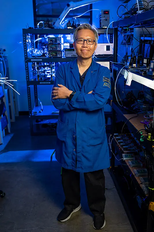 Nosang Myung stands with his arms crossed while standing in his lab with machinery and equipment around him.