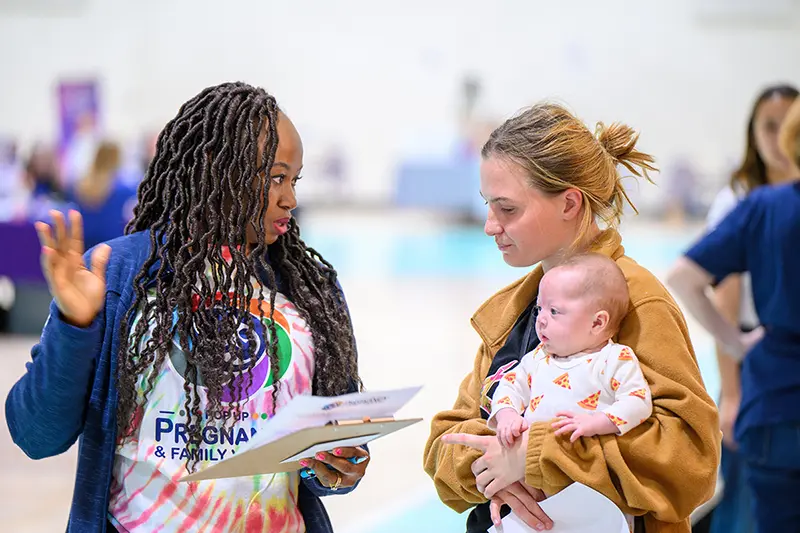 Joyce Adams talks to a young mother holding a baby at a Pop-Up Pregnancy & Family event.