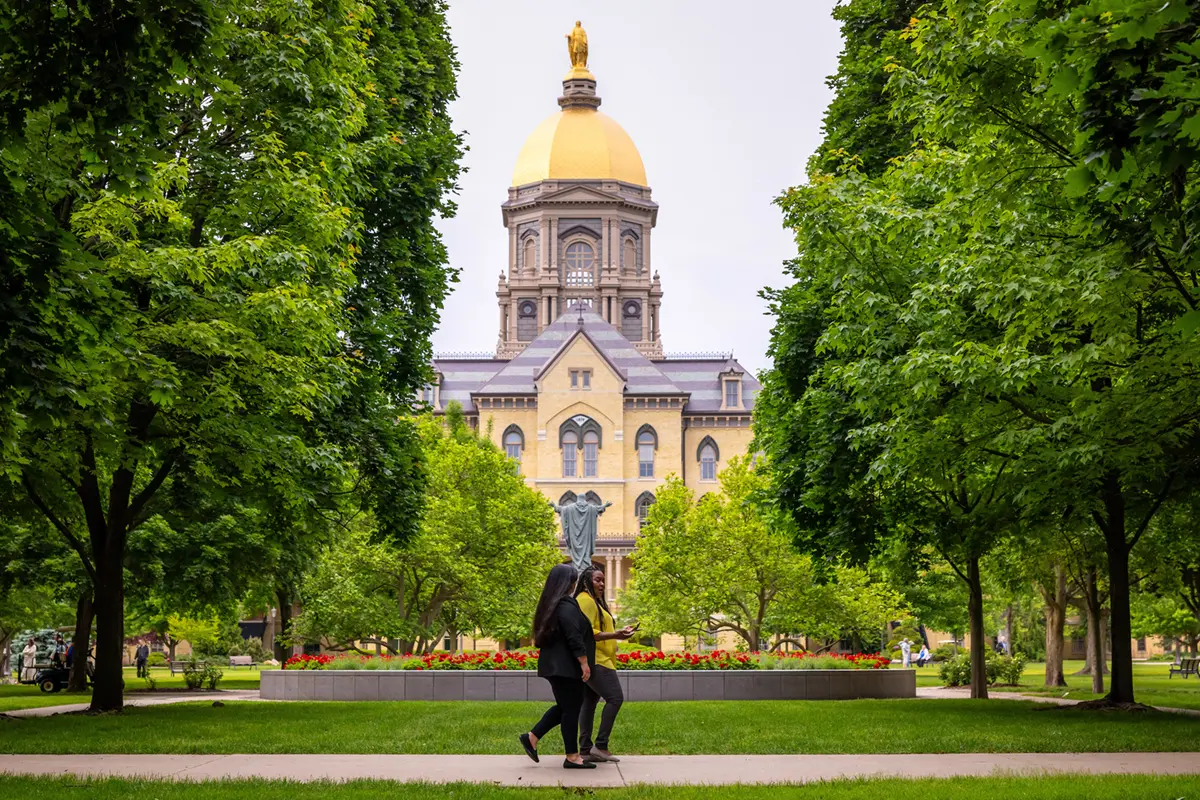 Two women walk along a sidewalk near the Main Building's Golden Dome on the University of Notre Dame campus.