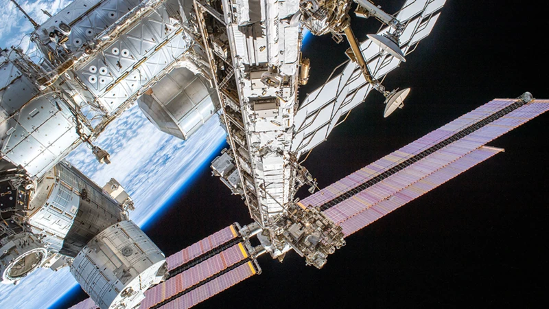 An exterior view of the International Space Station with its solar panels extending over the blackness of space and the blue Earth below.