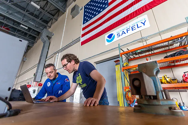 Joe Cione and David Richter work on a laptop in a hangar in Florida.