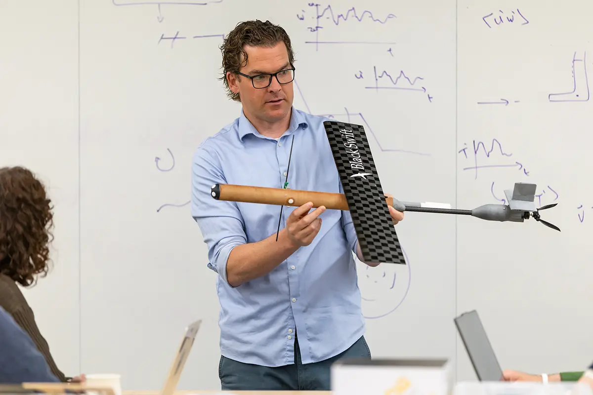 David Richter holding the drone in front of a dry-erase board speaking with students.