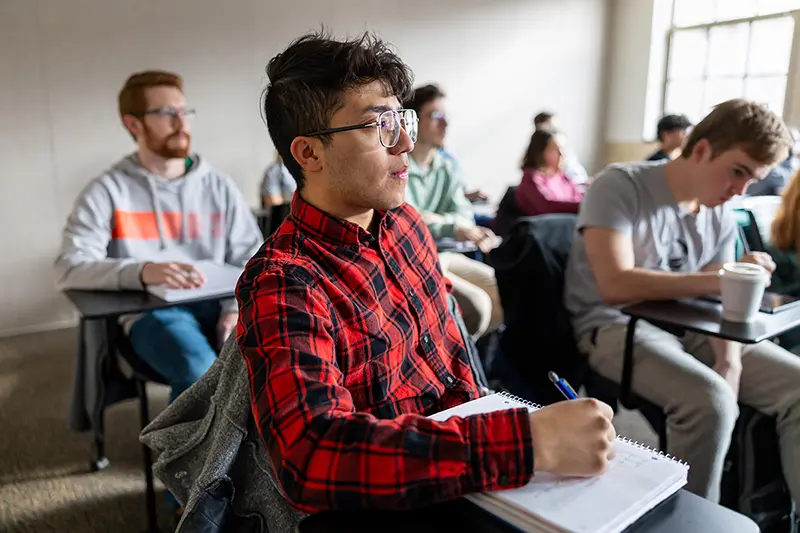 A male student listens to David Richter teaching a class with pen in hand.