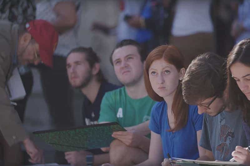 Students sketch as they look up at buildings in Rome.