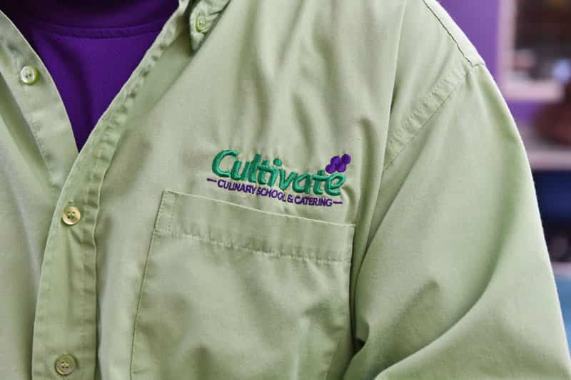 Cultivate Culinary logo embroidered on a green shirt.