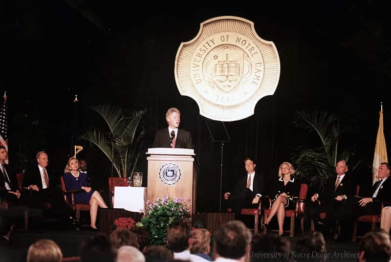 Bill Clinton speaks at a podium in front of a large University of Notre Dame gold seal.