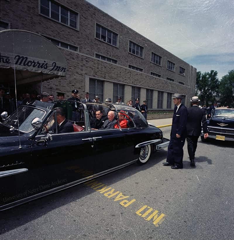 Hesburgh, Eisenhower and Cardinal Montini riding the backseat of a Studebaker car parked in front of the Morris Inn.