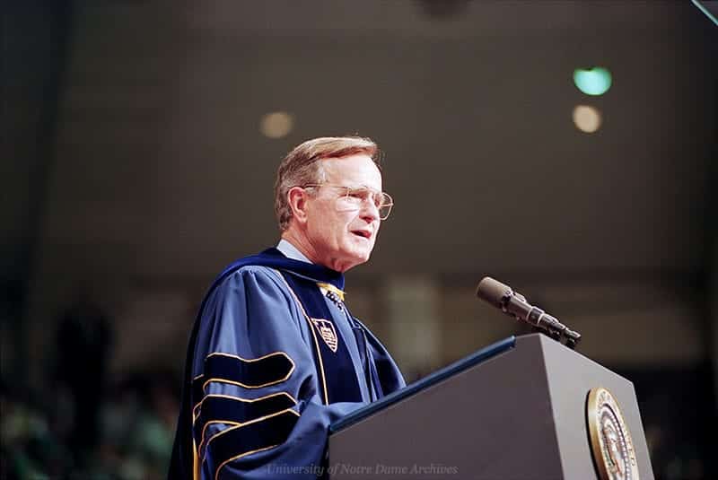 Bush speaks at a podium in graduation regalia.