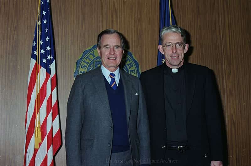 Bush and Monk Malloy smiles at the camera, posing beside an American flag.