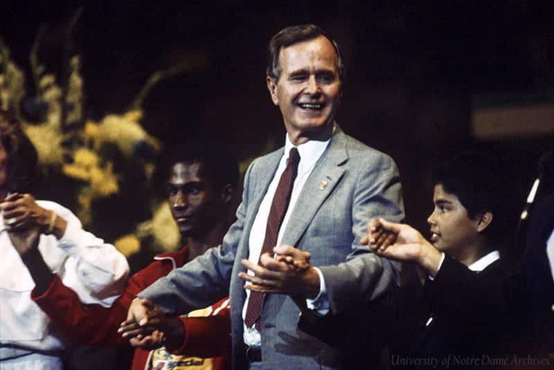 Bush holds hands with children, smiling.