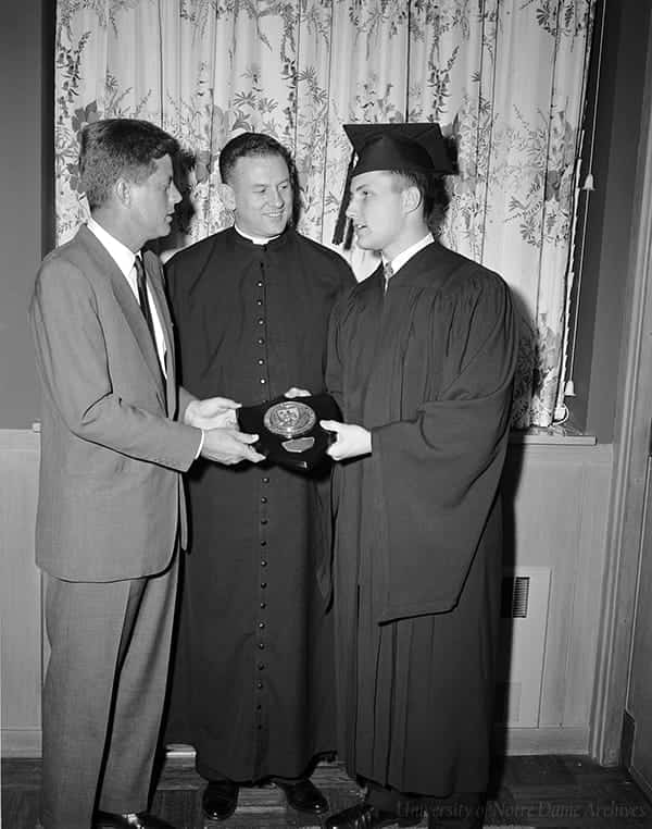 Kennedy shakes the hand of a student while accepting an award. A man stands between them smiling.