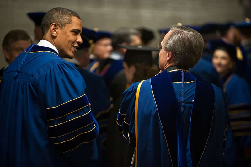 Rev. John Jenkins, C.S.C. and Barack Obama stand with their backs towards the camera wearing commencement robes.