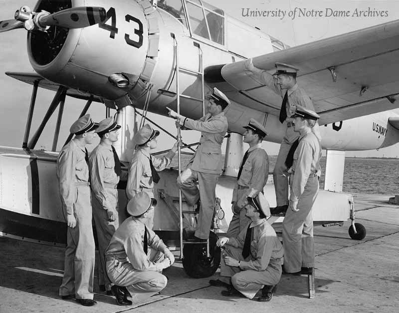 World War II (WWII) Naval Air Training, c1941. A group of Aviation Cadets, former students of Notre Dame, examining a Navy seaplane airplane on an aircraft carrier.