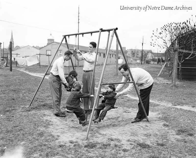 Three male students playing with their children on a playground at Vetville, c1955.