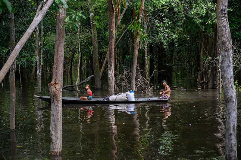 Two people on a boat in a flooded area carry bags full of farinha.