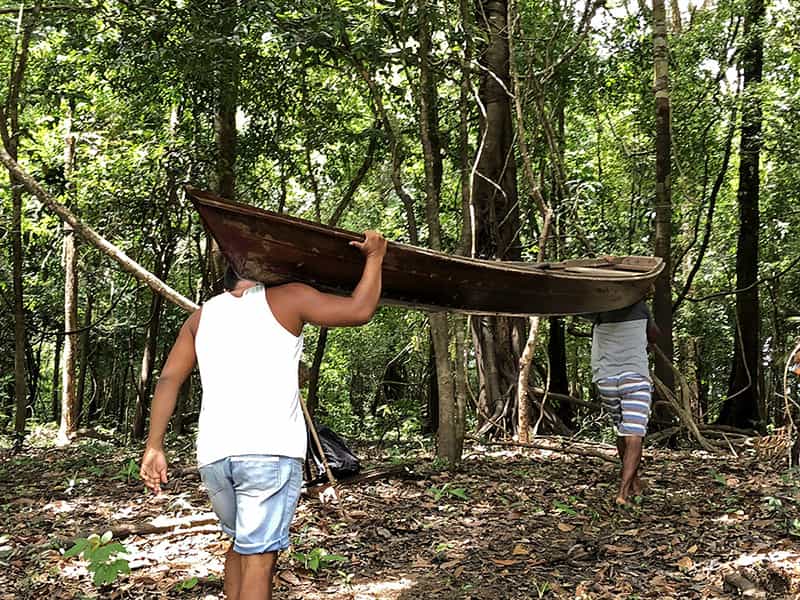 Two men carry a canoe on their shoulders through a wooded area.