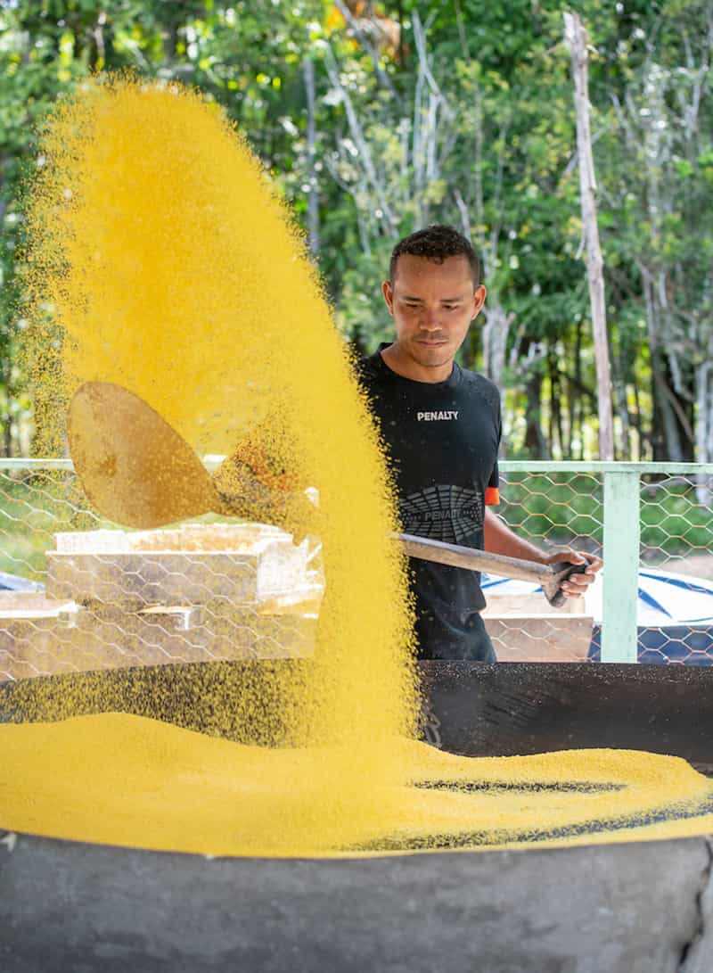 A man toasts the dried flour on a large firepit frying pan.
