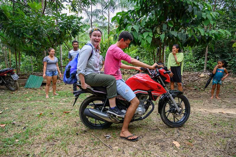 A student sits on the back of a moterbike making a terrified face as others in the back smile and laugh.