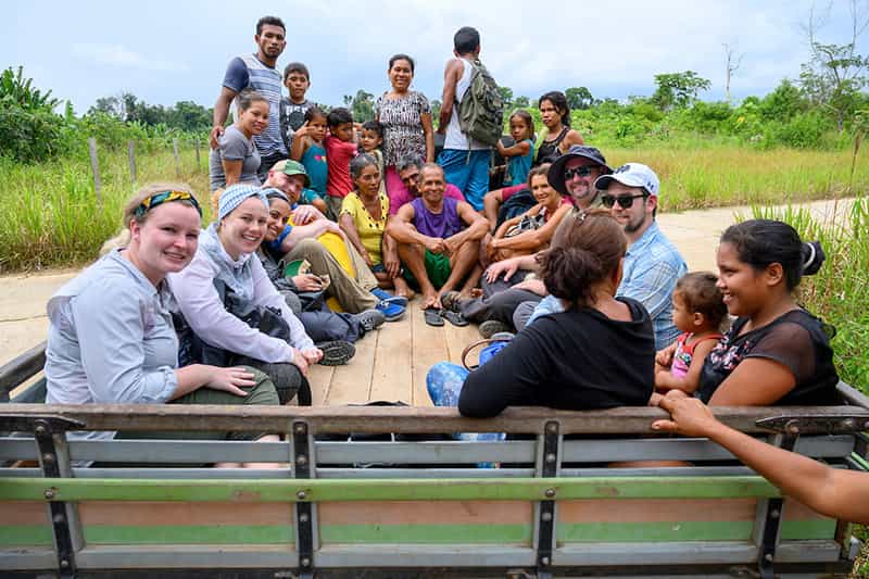 A large group of people sit on the back of a truck in an open field.