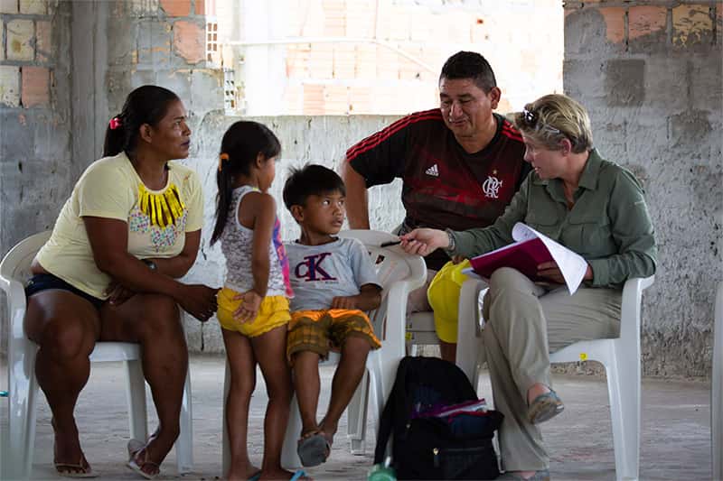 A woman with a notebook and pen in hand talks to a family.