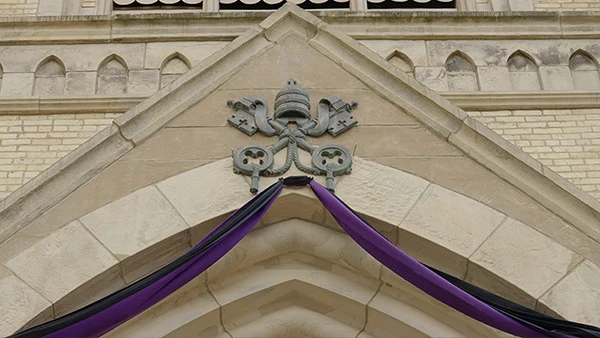 Papal symbol above an archway draped with purple and black fabric.