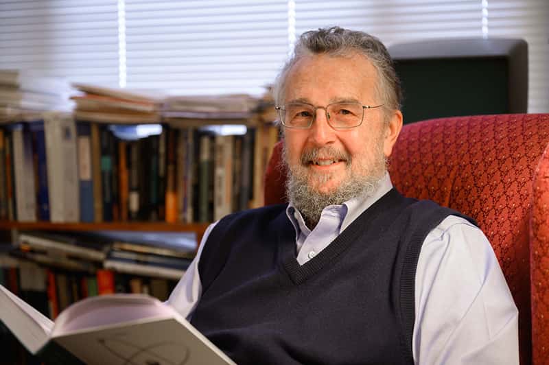 A man sits in a red armchair reading a physics textbook.
