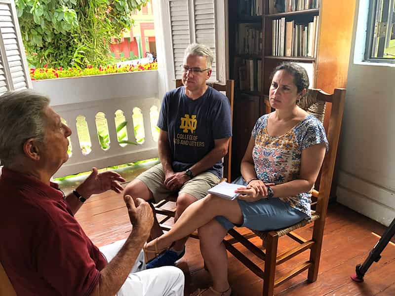A man and a woman interview another man sitting on a porch.