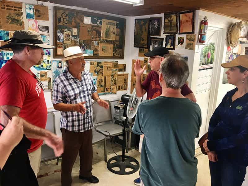 People stand and talk inside a room where the walls are covered in artwork, newspaper clippings, and photography.