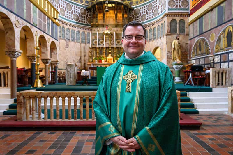 A priest stands for a photo inside of a church.