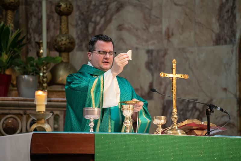 A priest stands for a photo inside of a church.