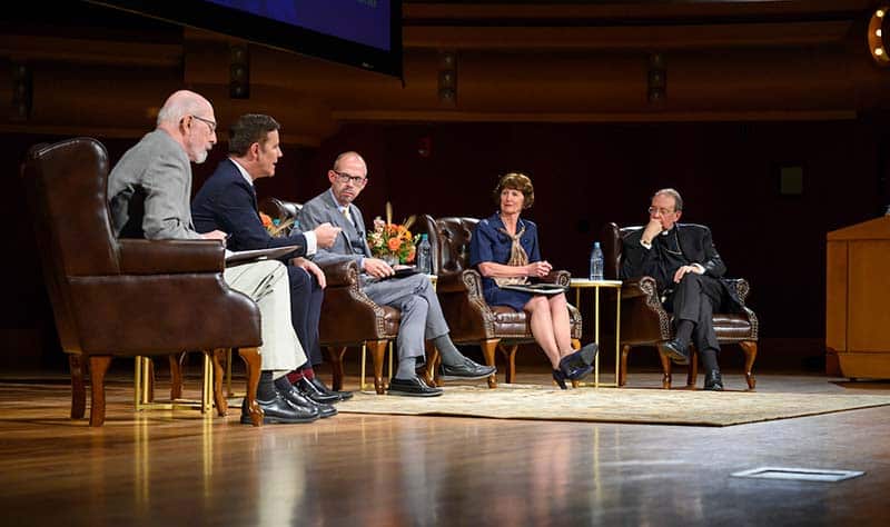 Five people sit in chairs on a stage.