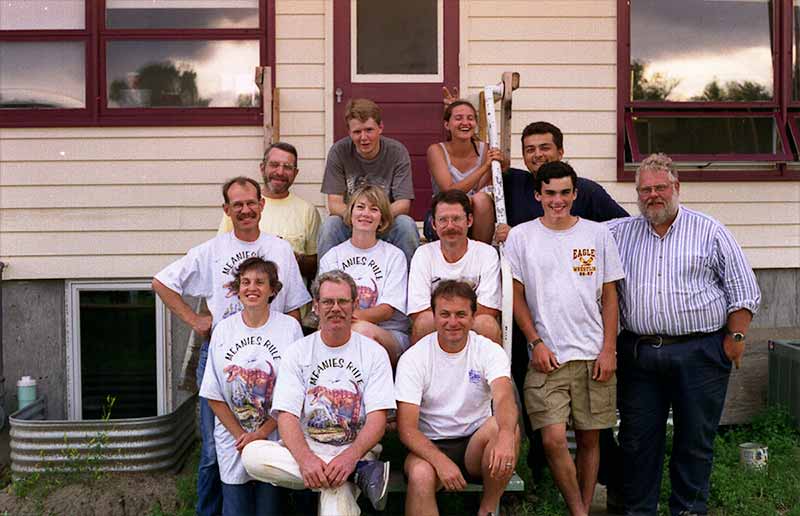 A group of twelve people, including students and	Keith Rigby pose for a photo sitting and standing next to building.