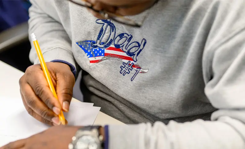 A close up hands holding a pencil, writing on a sheet of paper.
