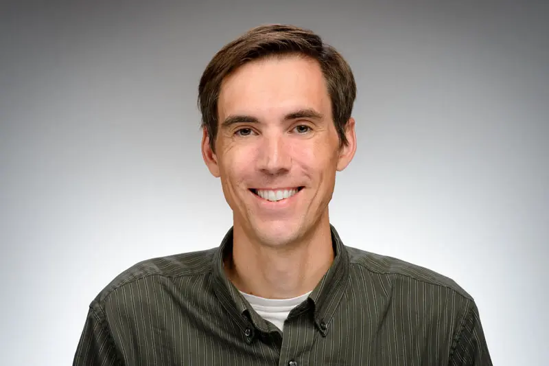 A headshot of David Phillips in a dark green button down shirt.