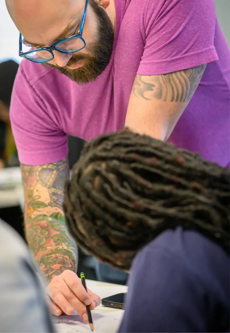Phil Dejean, in a pink shirt, leans over a student to help her with her homework.