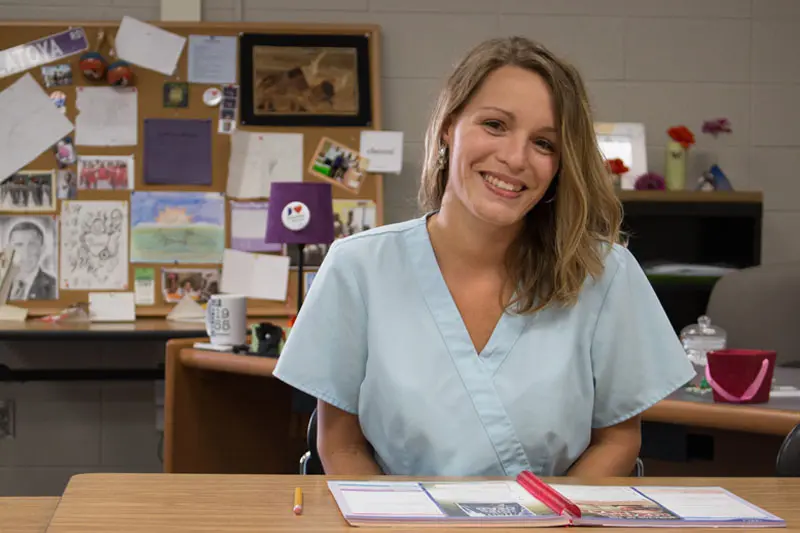 Katie Reigelsperger sits at a desk, wearing light blue scrubs.