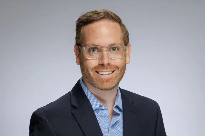 A headshot of Patrick Turner wear a light blue button down shirt under a navy sport coat.
