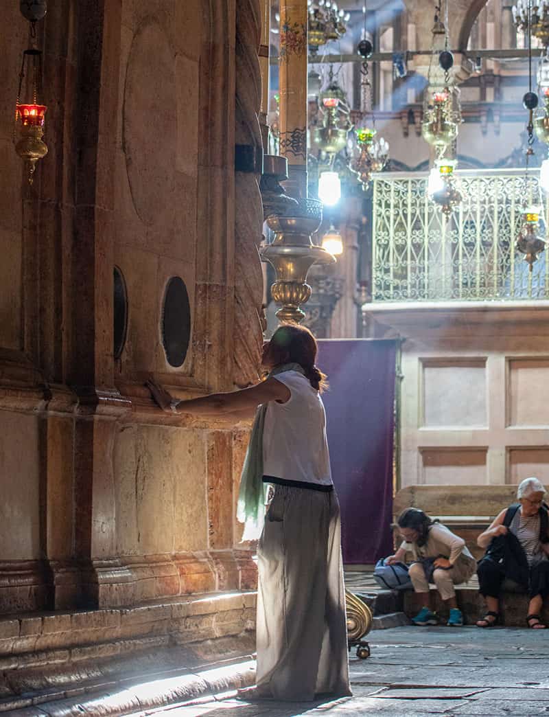 A woman rests her hands on a wall and prays.