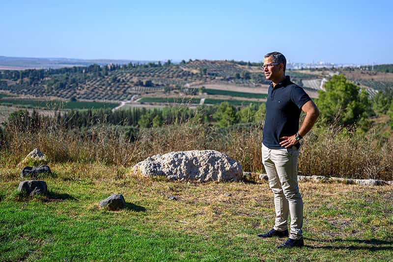 A man, with his hands on his hips, stands looking out in the distance surrounded by beautiful landscape.