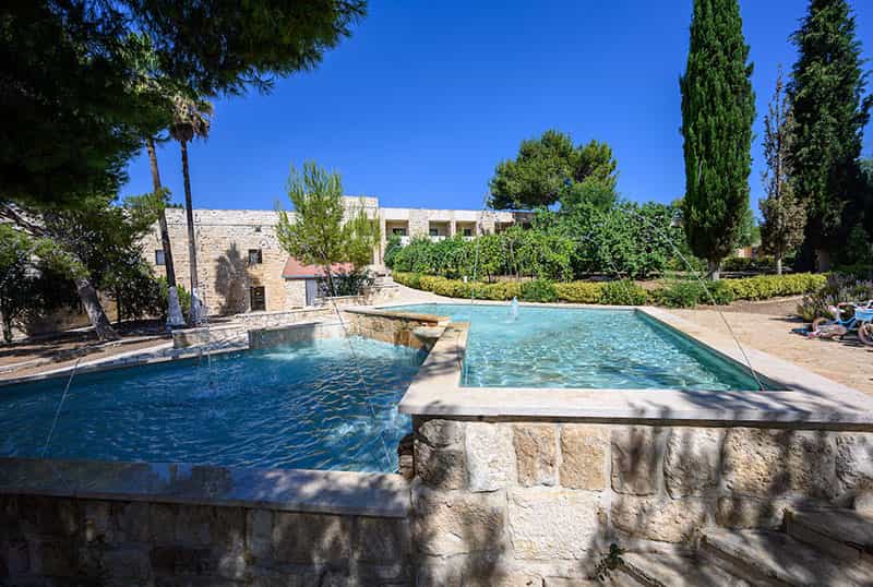 Two level water fountain in a courtyard, trees and a building sits in the background.
